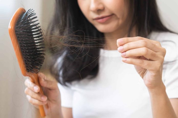Serious asian young woman holding brush holding comb, hairbrush with fall black hair from scalp after brushing, looking on hand worry about balding. Health care, beauty treatment, hair loss problem.